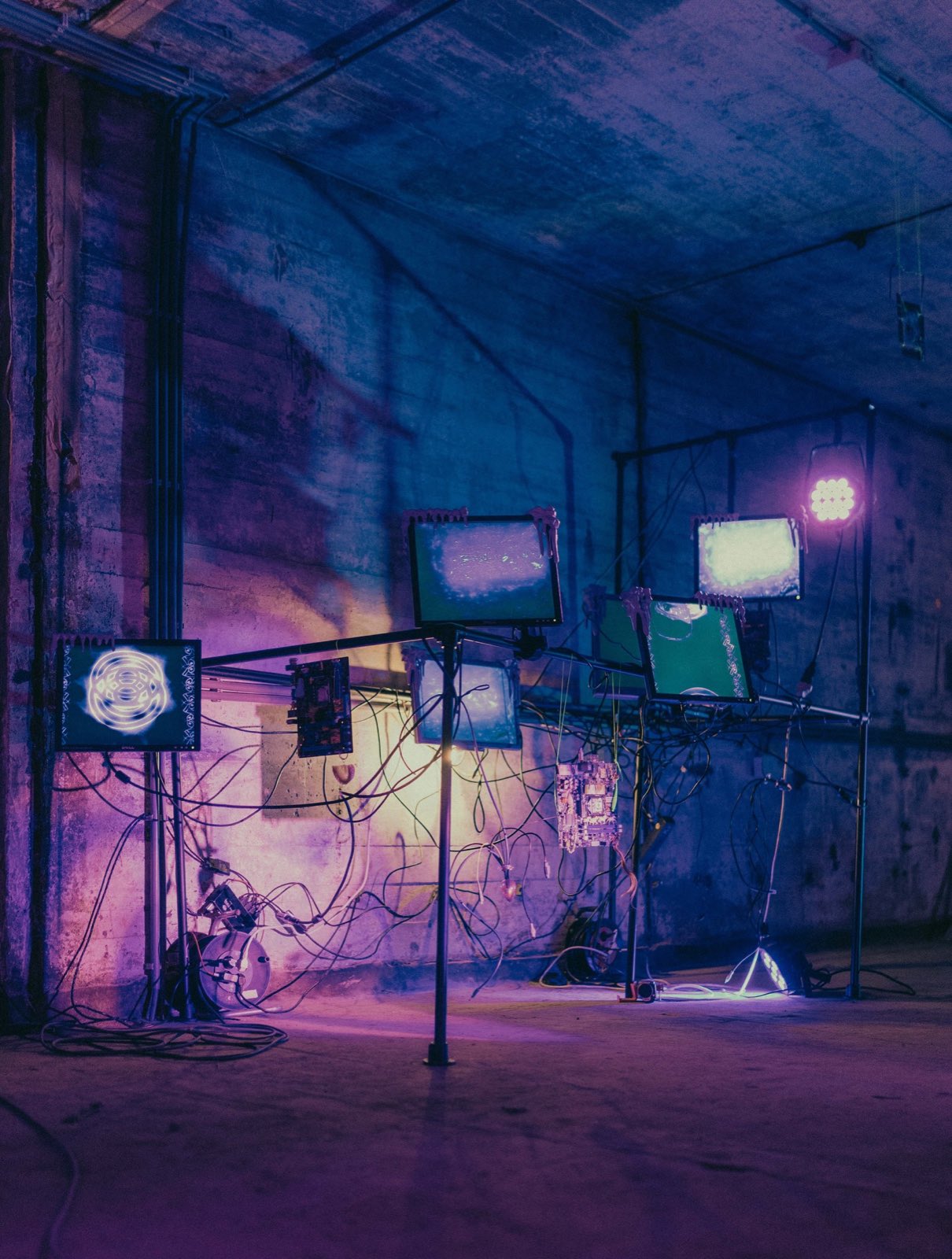 dreaming in the ruins of big tech, gesloopte monitoren op een steigerrig in een betonnen hal